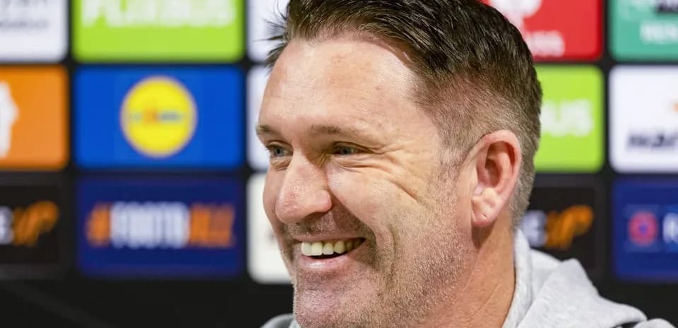 Manager smiling at press conference with logos in background
