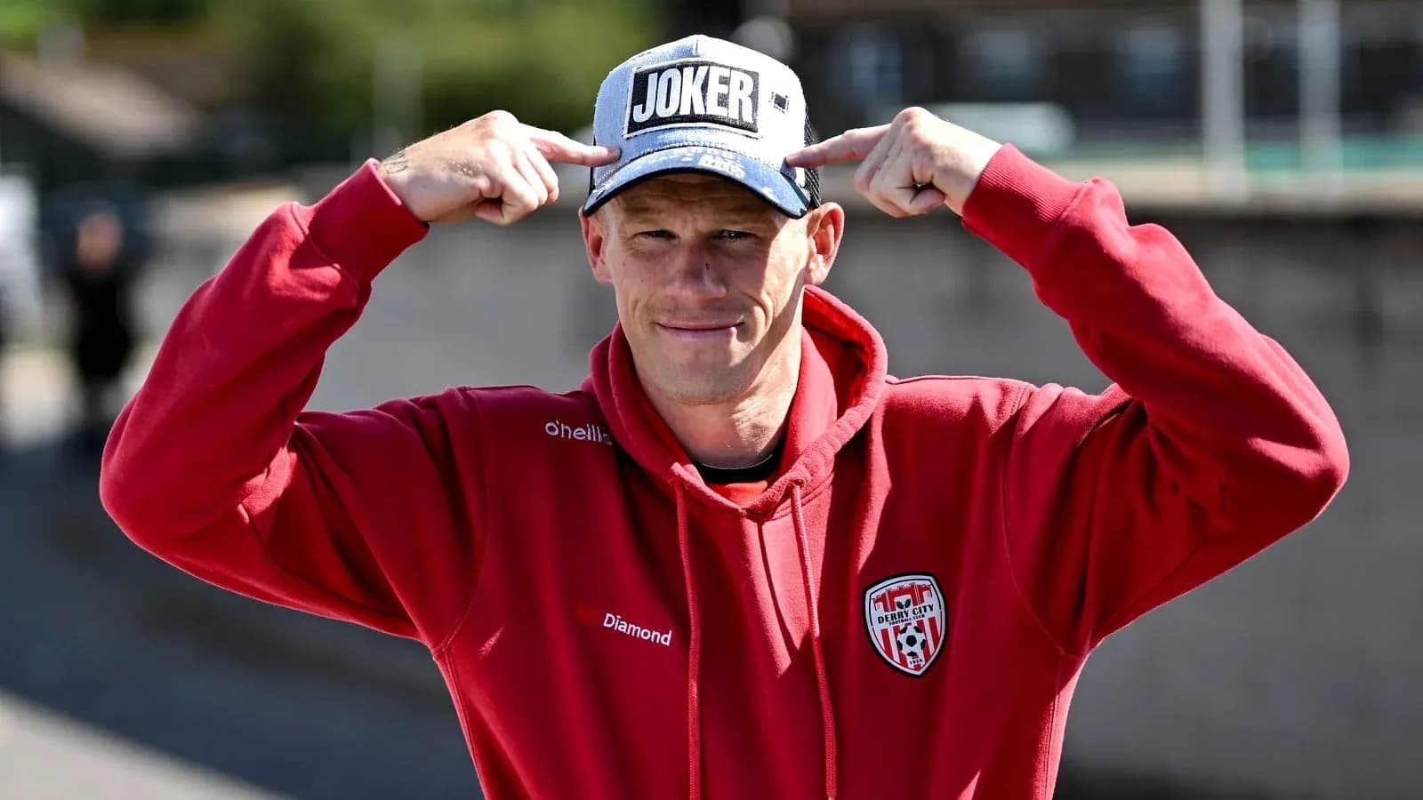 Man wearing 'JOKER' cap and red hoodie