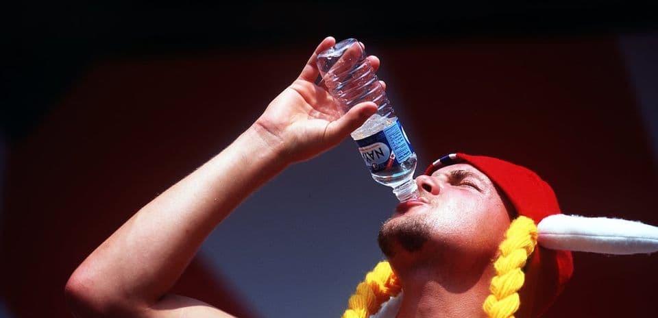 Person drinking water from a bottle, wearing a hat