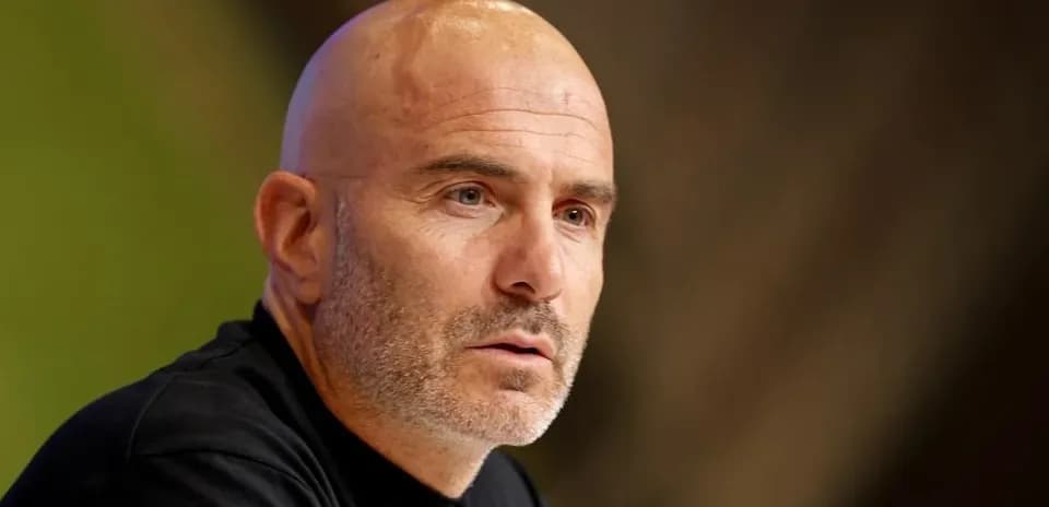 Coach speaking at press conference with focused expression