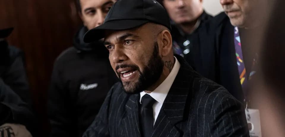 Man speaking to crowd, wearing a suit and cap
