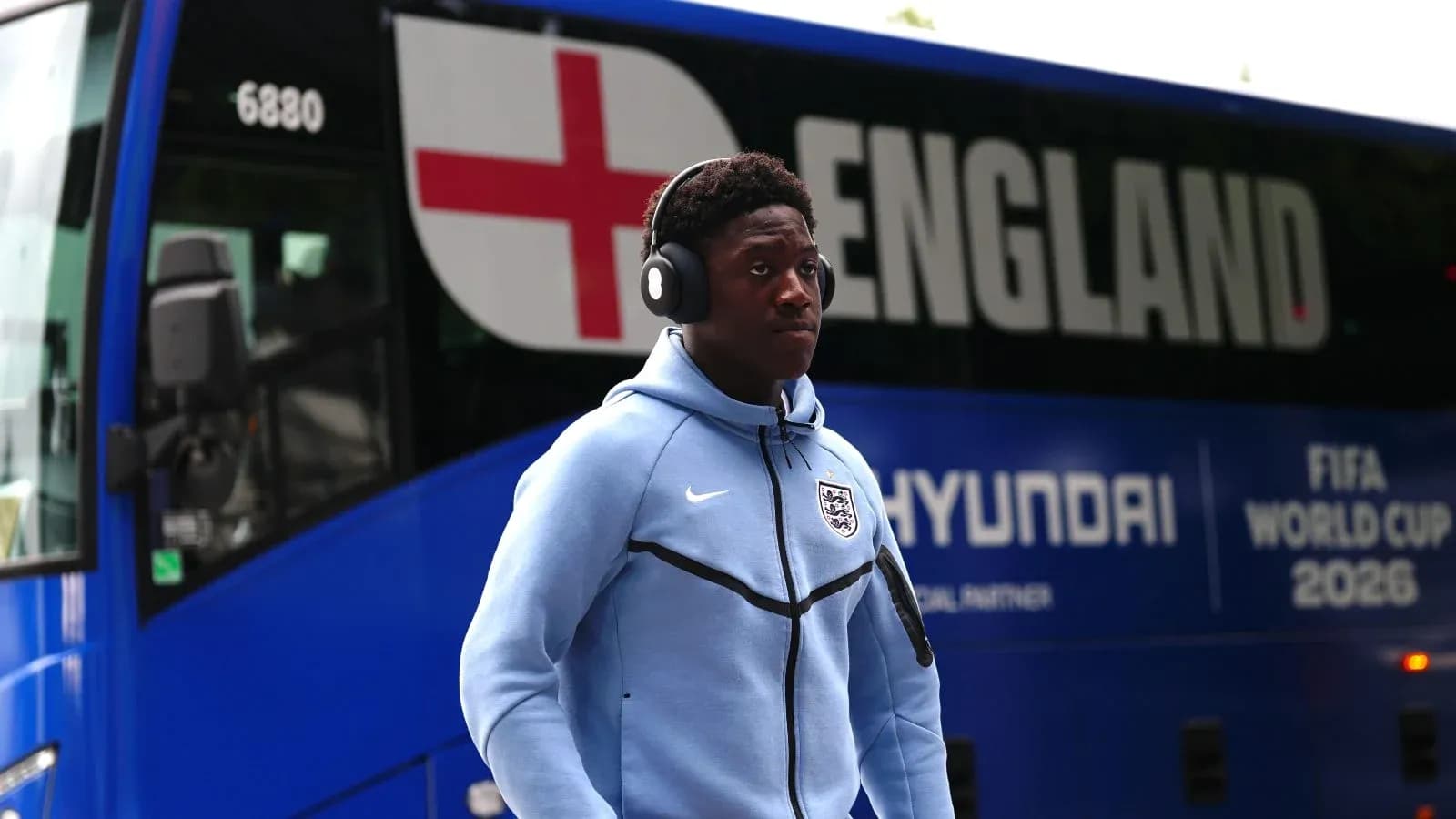 Player wearing headphones walking past England team bus