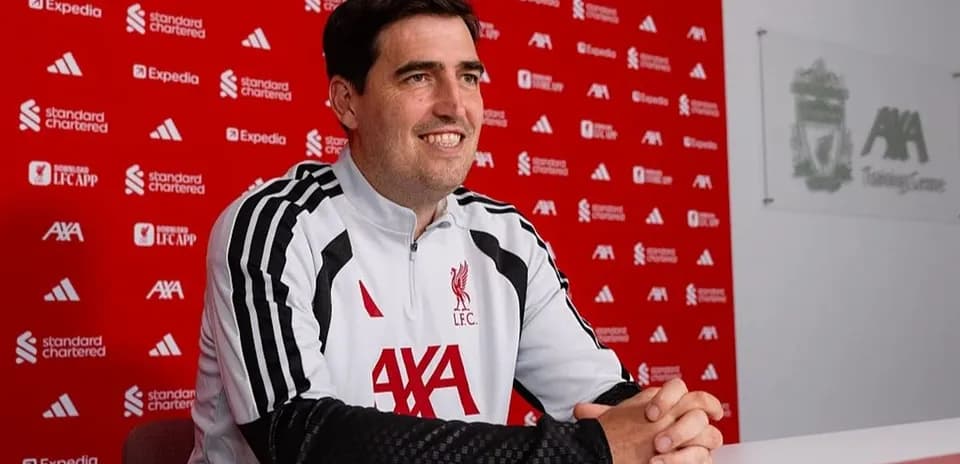 Coach sitting at press conference table with Liverpool backdrop