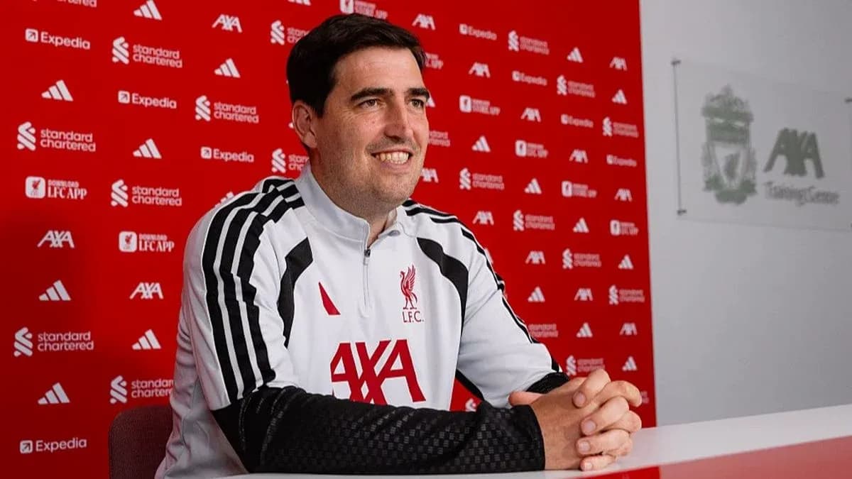 Coach sitting at press conference table with Liverpool backdrop