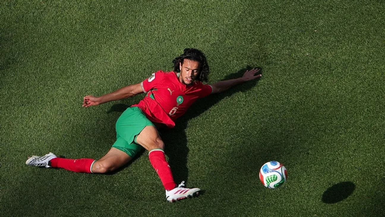 Player in red and green uniform reaching for soccer ball