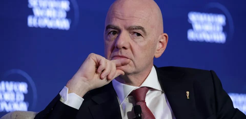 Man speaking at a conference with FIFA logo pin