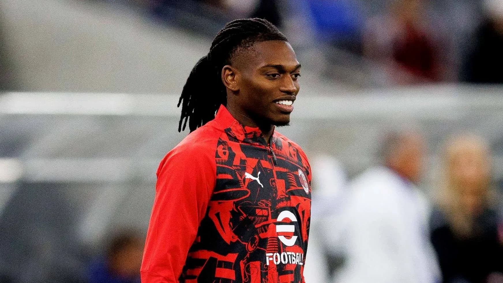 Player in red warm-up jacket smiling during training