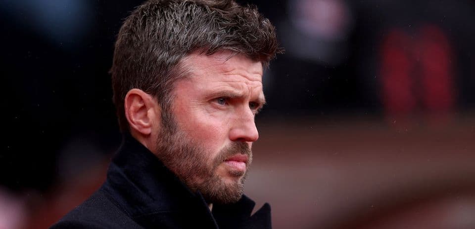 Man in black coat observing match from sidelines