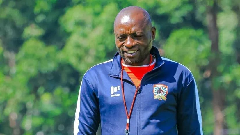 Coach walking on training ground with trees behind