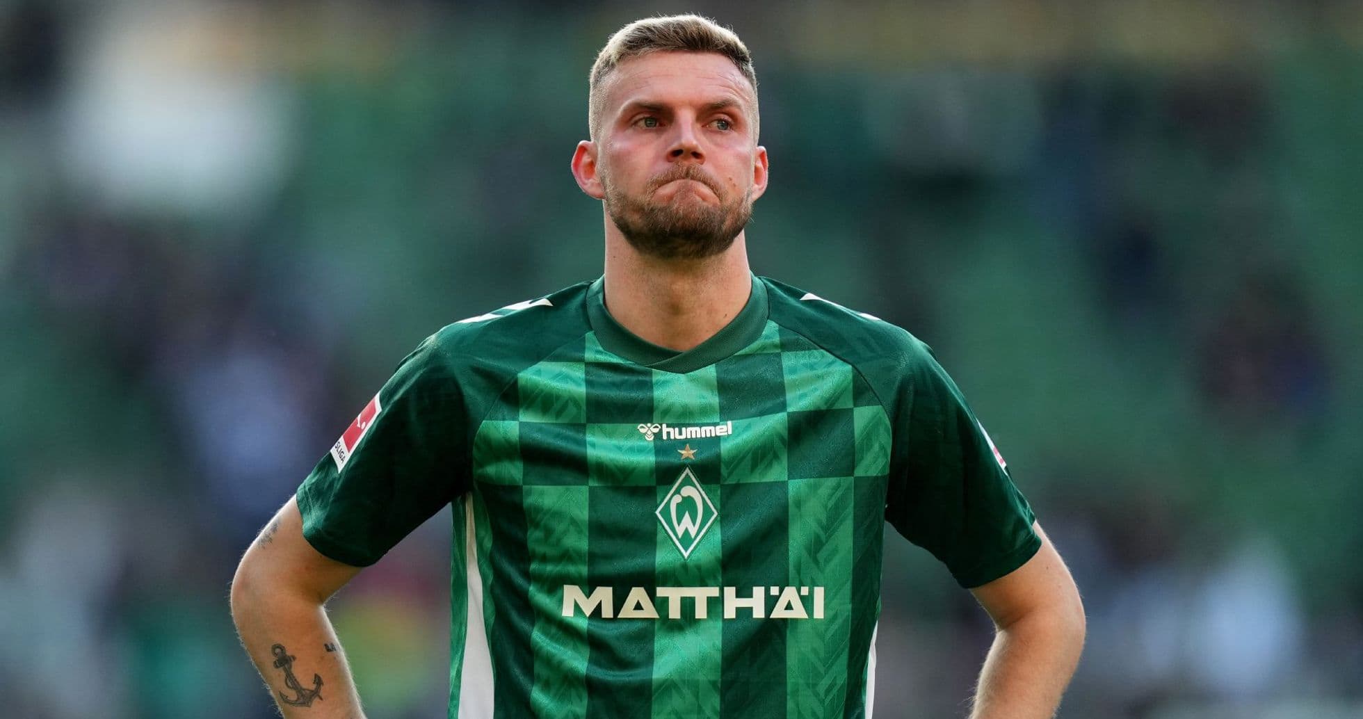 Player in green jersey looking down on the pitch