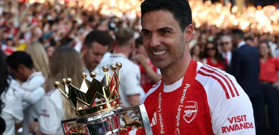 Arsenal manager holding Premier League trophy on pitch