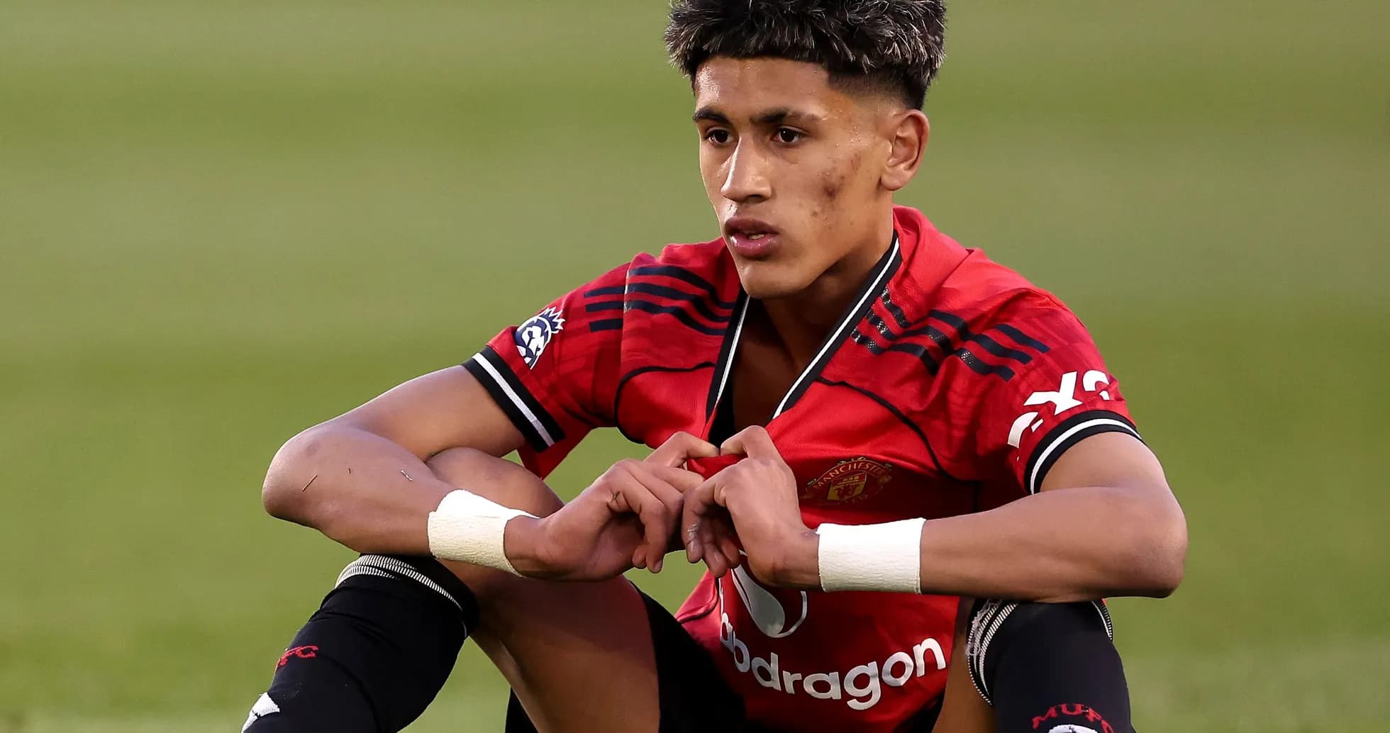 Young player sitting on field in Manchester United kit
