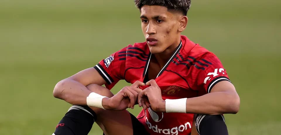 Young player sitting on field in Manchester United kit