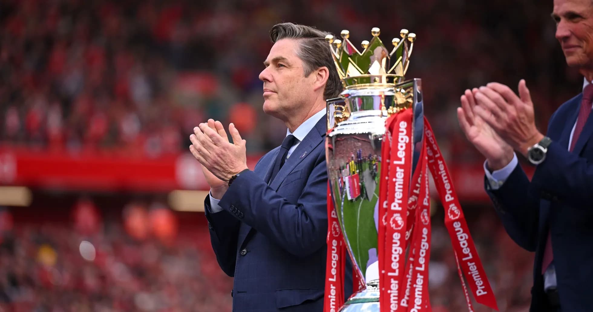 Man applauding next to Premier League trophy
