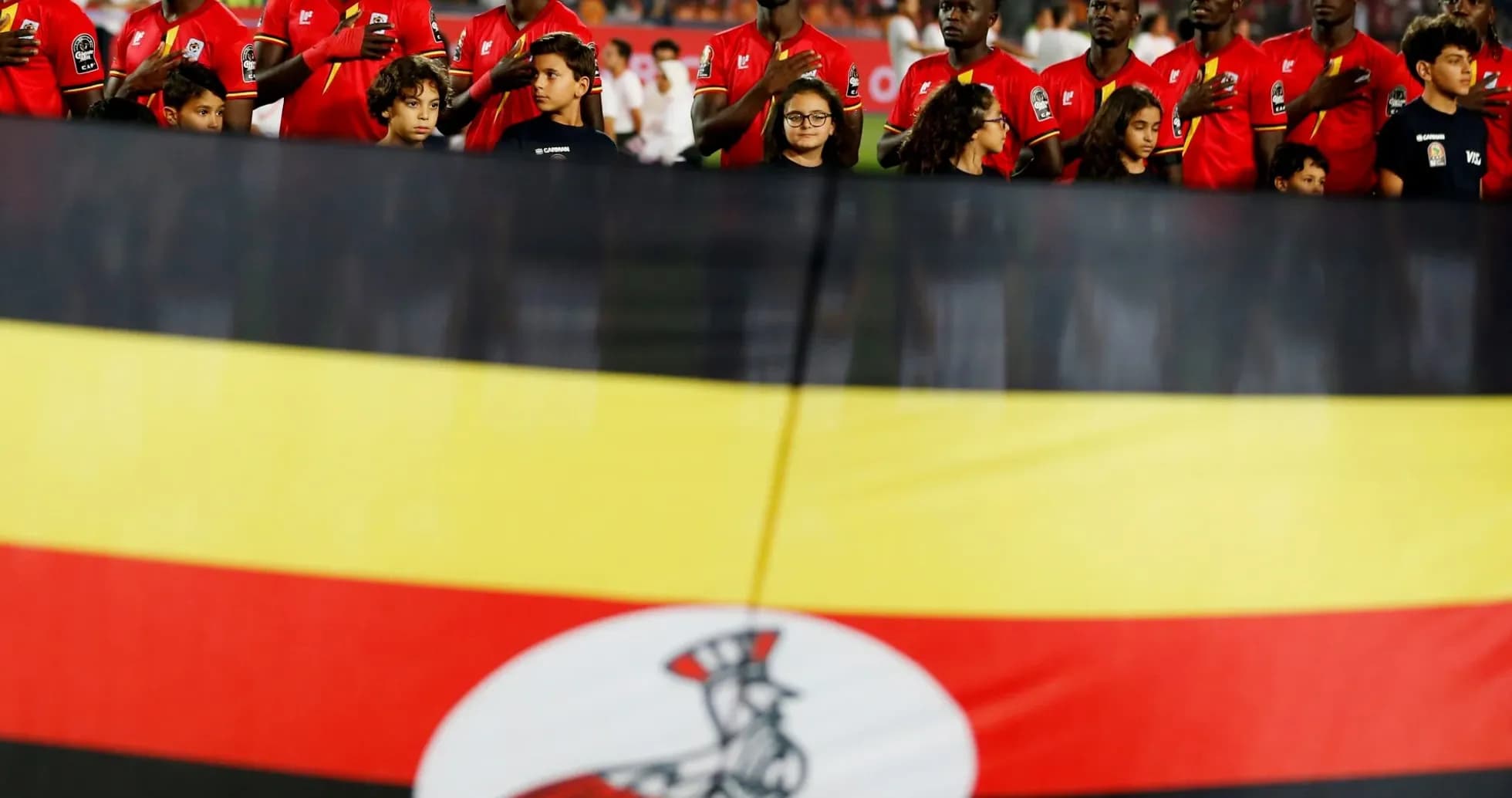Ugandan team members singing national anthem with flag