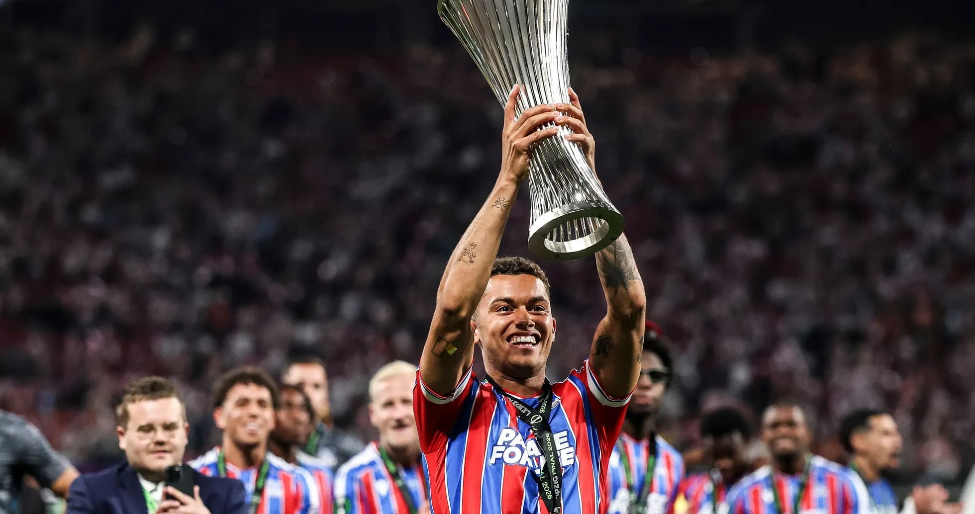 Player celebrating with trophy in stadium crowd