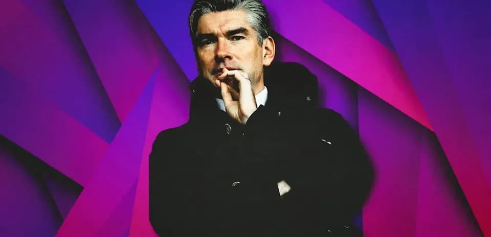 Man in coat with hand to mouth against colorful background