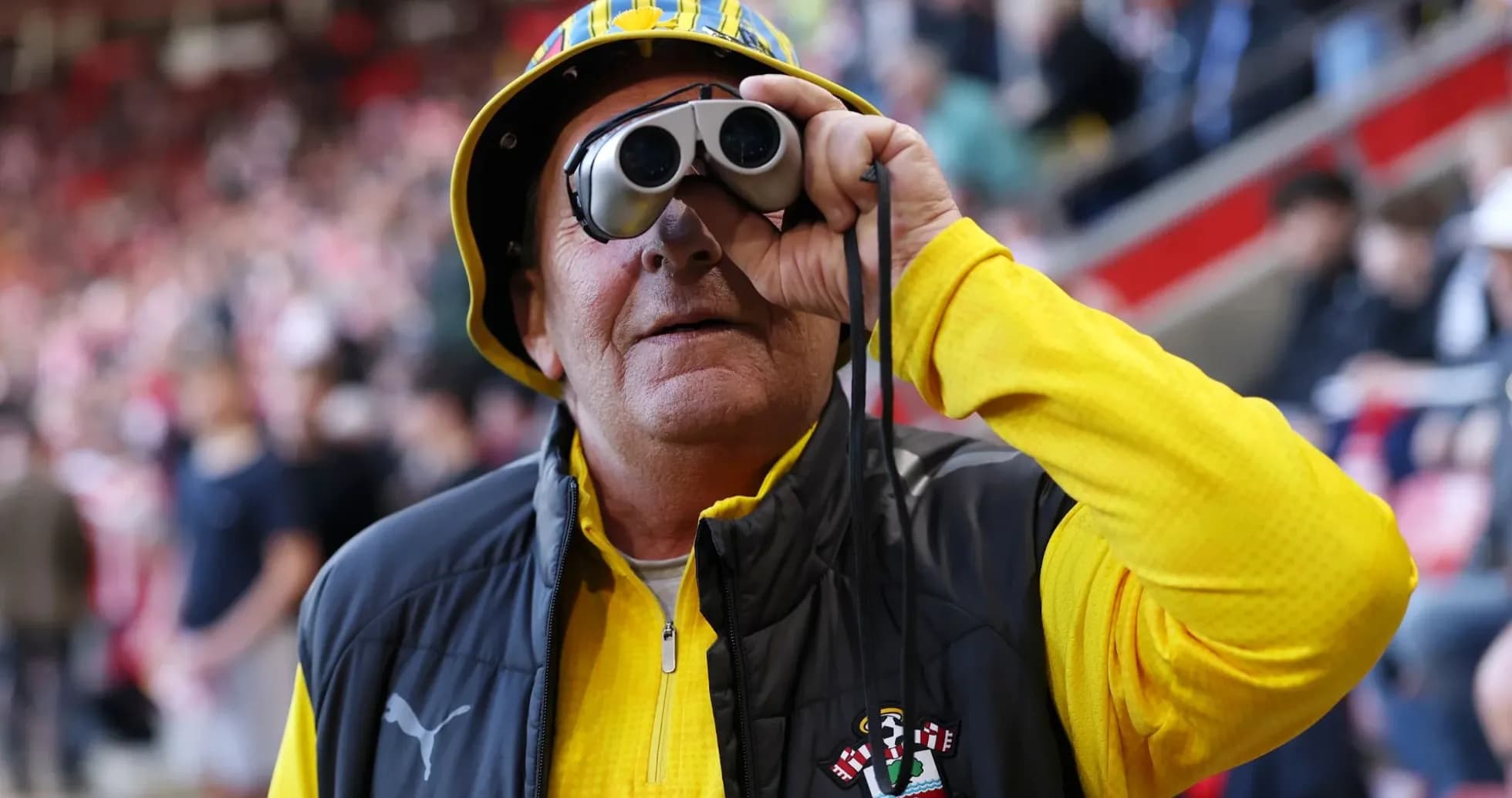 Fan wearing binoculars and a hat at stadium