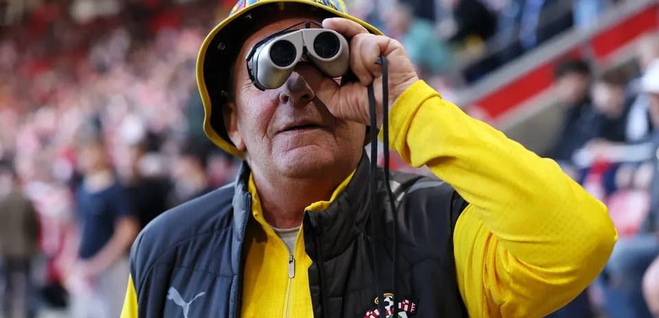 Fan wearing binoculars and a hat at stadium