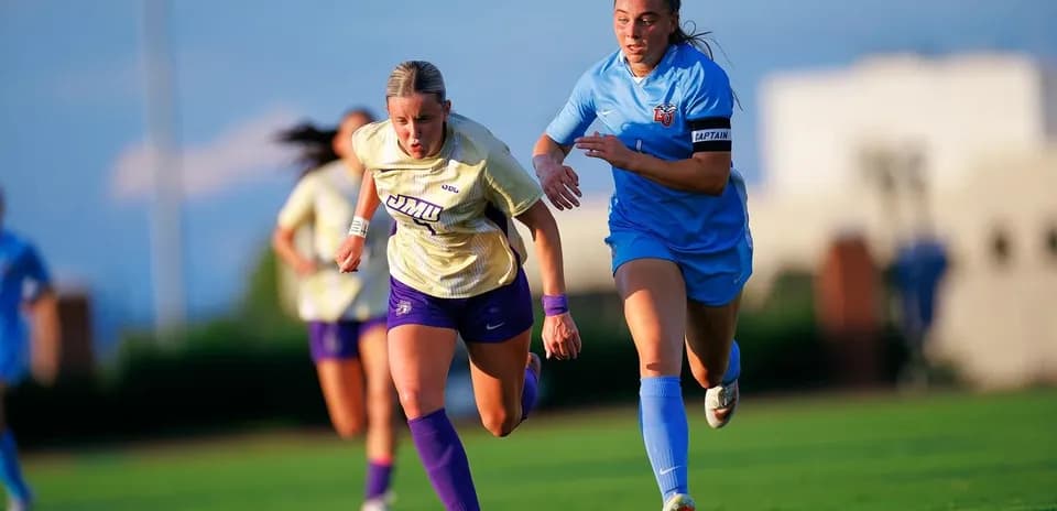 Two soccer players racing for the ball on field