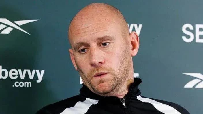 Coach speaking at press conference with serious expression