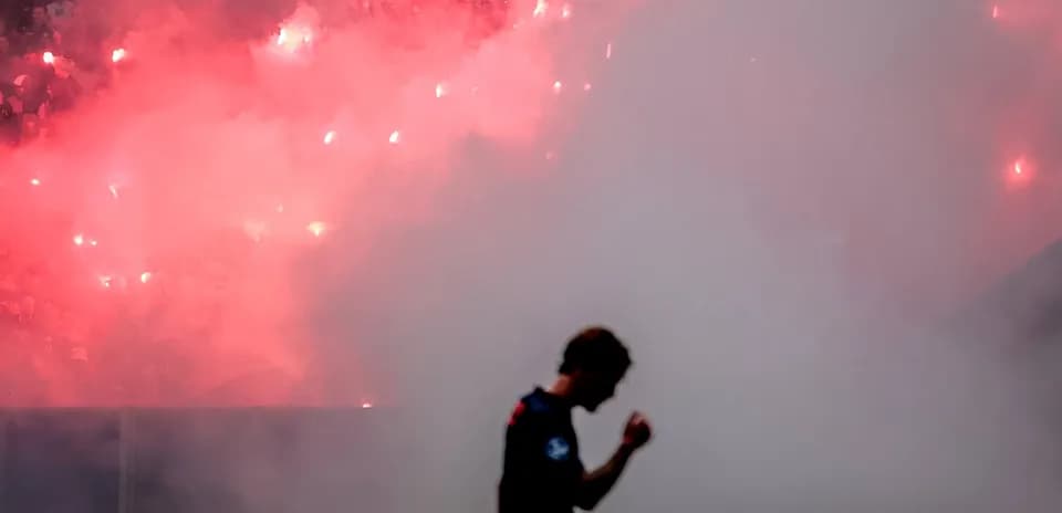Player celebrating amid smoke and flares in stadium