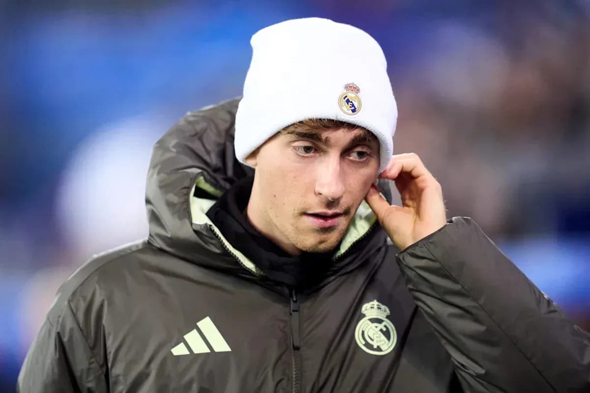 Player wearing Real Madrid jacket and beanie on pitch