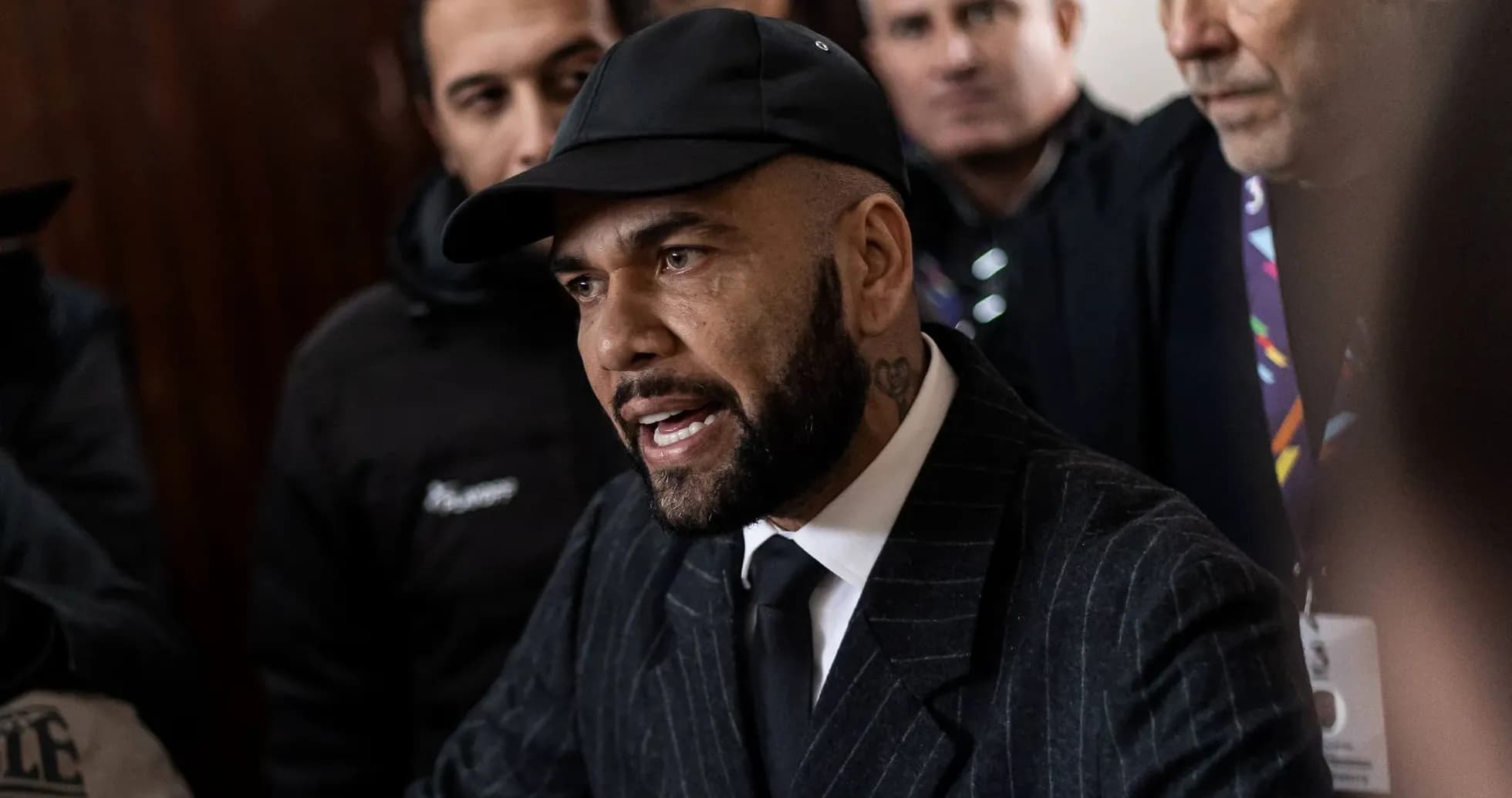 Man speaking to crowd, wearing a suit and cap Man speaking to crowd, wearing a suit and cap