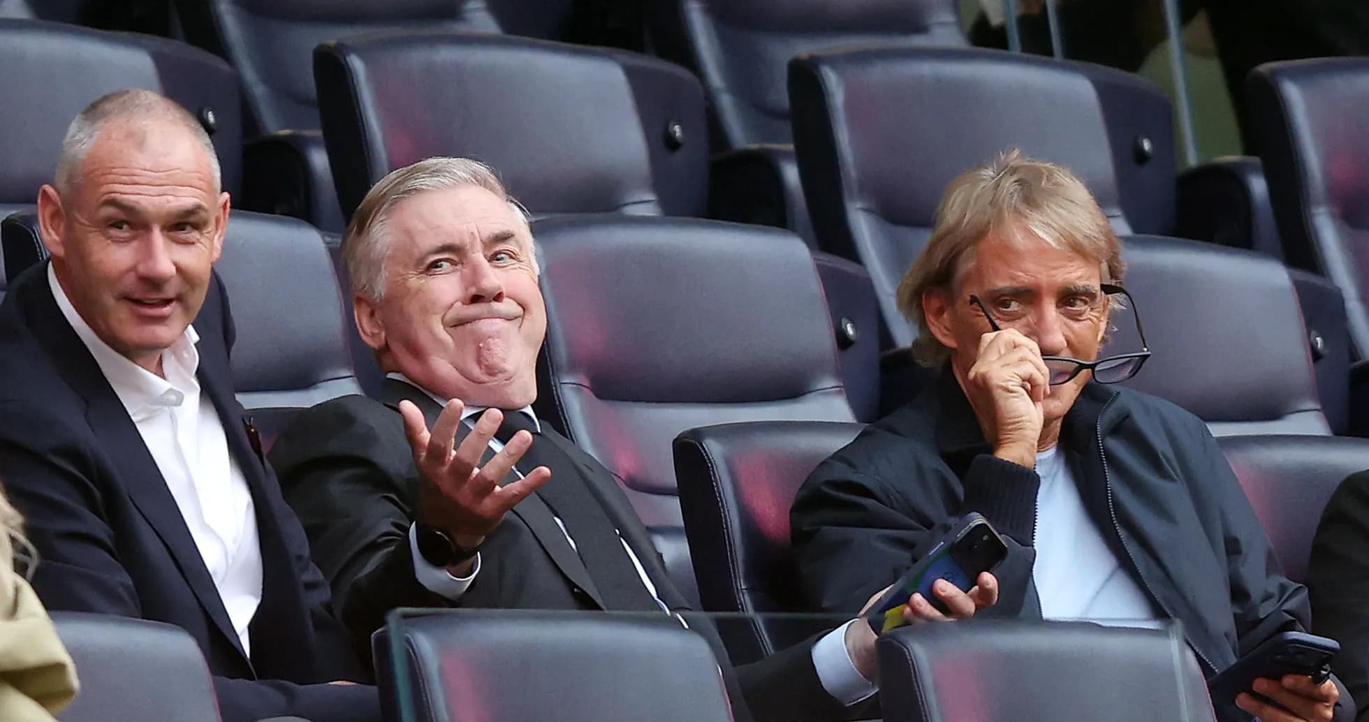 Three men seated in stadium, discussing match Three men seated in stadium, discussing match