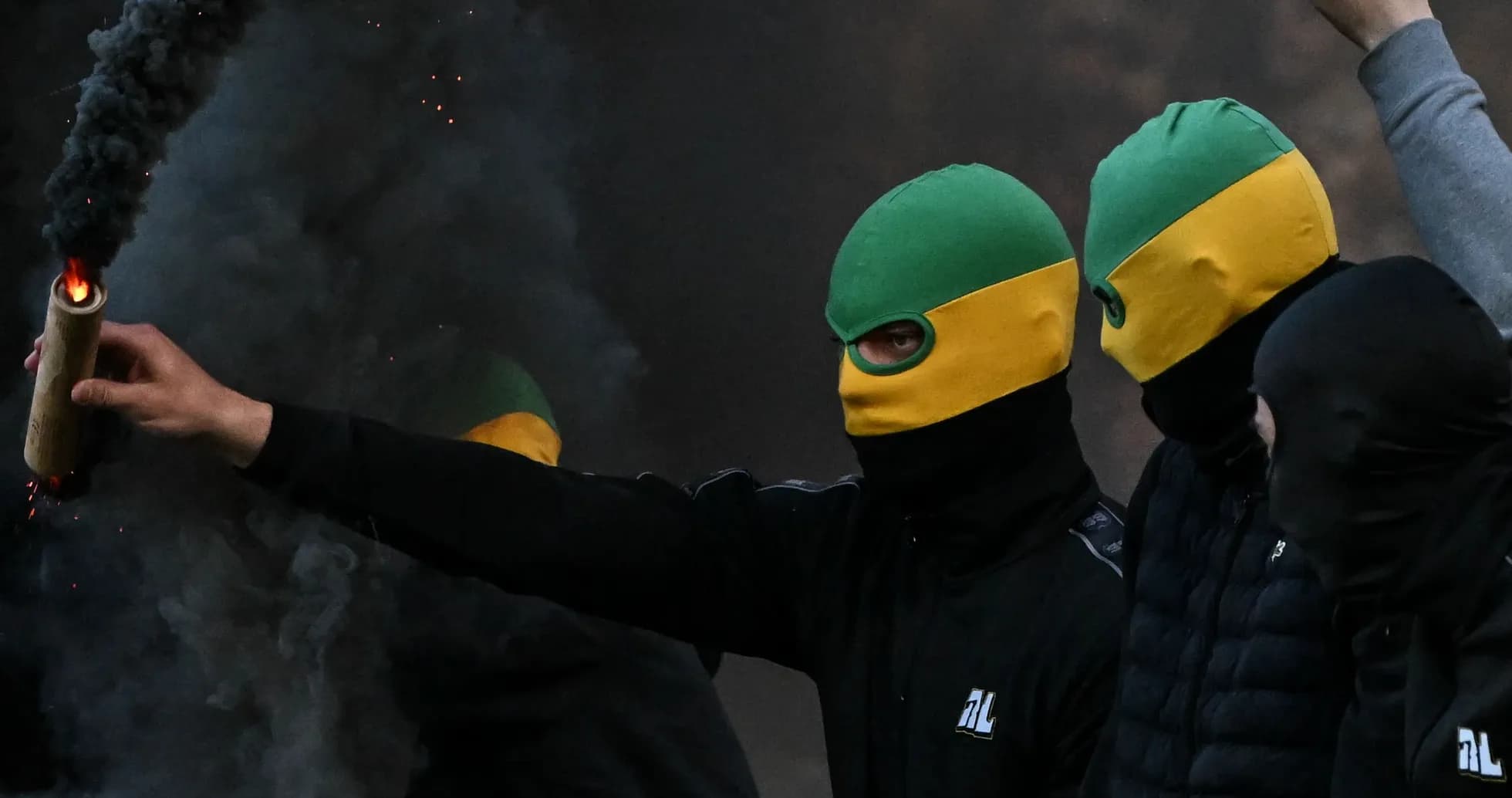 Masked individuals holding a flare amid smoke Masked individuals holding a flare amid smoke